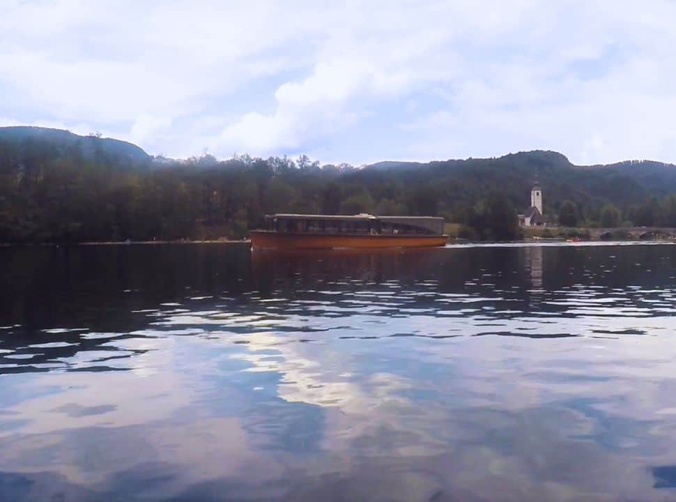 a tour boat on the water at Lake Bohinj with in the background the church at Ribčev Laz Slovenia