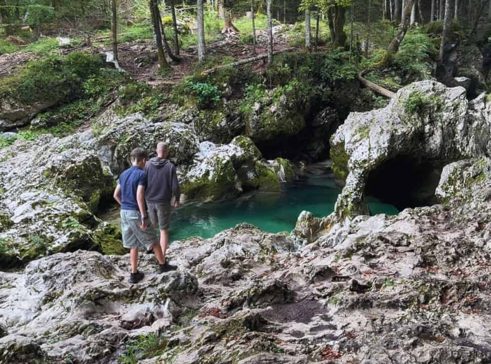 father and son walking along the rocks nearby a crystal clear pool set around beautiful rock formations in a forest at Mostnica Gorge near Lake Bohinj Slovenia 