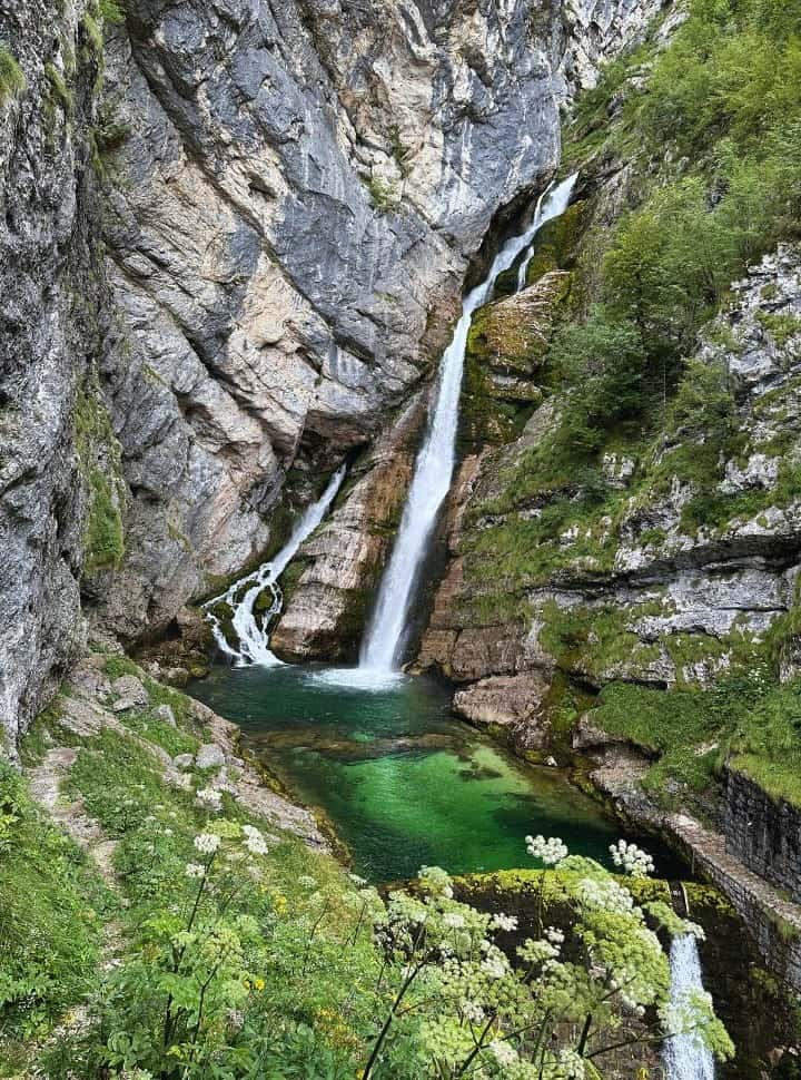 a waterfall falling into a green crystal clear pool with a river flowing down through the rocks at Savica Waterfall Bohinj Lake