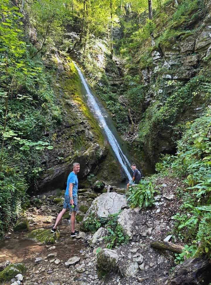 father and son at a small waterfall surrounded by rocks and lush vegetation in Slovenia Koseška Gorge