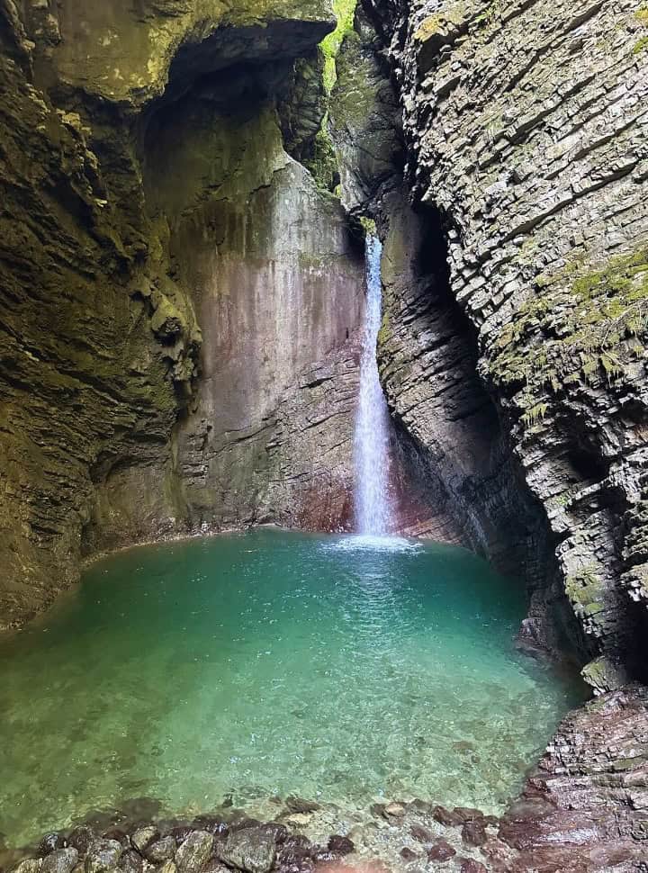 waterfall set within a cave, tumbling down in a crystal clear emerald green waterpool at Kozjak Waterfall, Slovenia