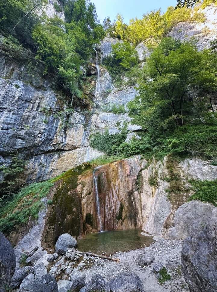 small waterfall surrounded by rock walls, vegetation and bolders in slovenia