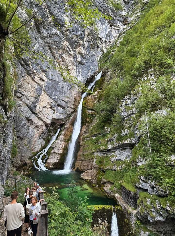 group of people stading near an iron gate to stand close to the savica waterfall for a picture. near Bohinj Lake