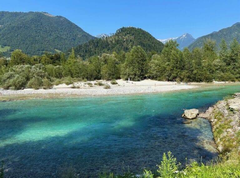view of a emerald blue and green river with a white rocky river bank beach and mountains in the background in Tolmin Slovenia