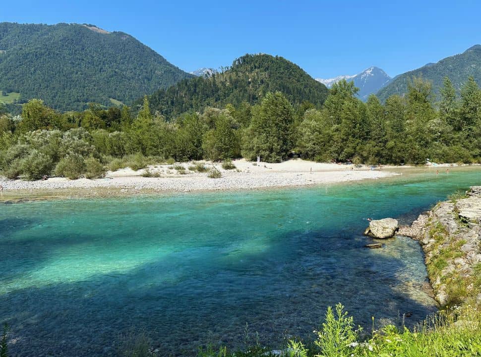 view of a emerald blue and green river with a white rocky river bank beach and mountains in the background in Tolmin Slovenia