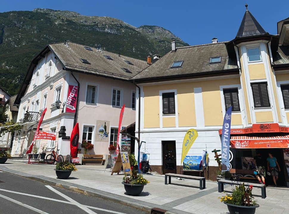 traditional buildings set along a main street in Bovec Slovenia, tour companies are located within these buildings, with in the background there are mountains