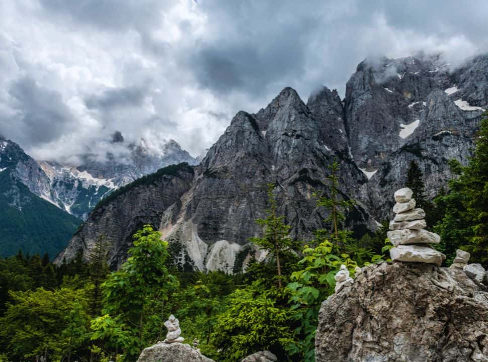 views of mountain range seen from a mountain pass, clouds cover the top slightly, people have piled rocks along the road in Slovenia