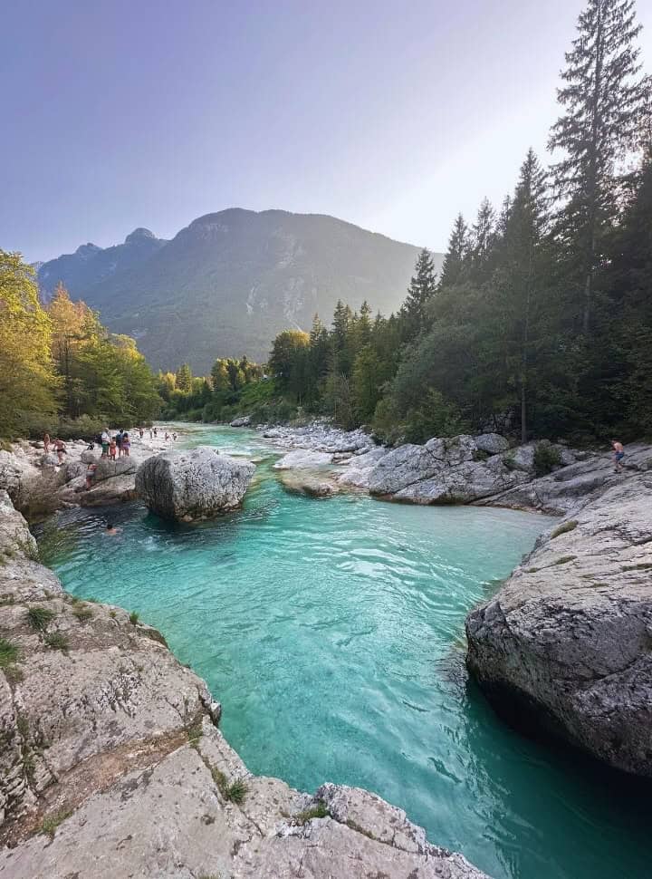 stunning creamy blue riverpool water surrounded by white lime stones together with pine trees, mountain seen along the horizon