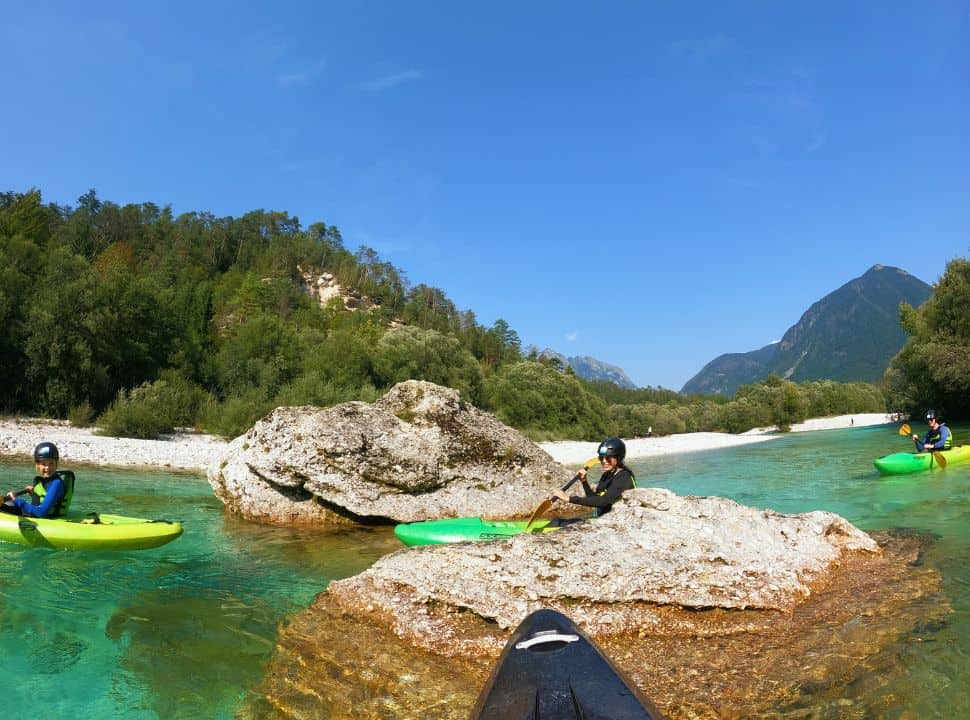 family of three enjoying a kayak tour at the Soča River, woman kayaking between two boulders, mountains and green vegetation in the back
