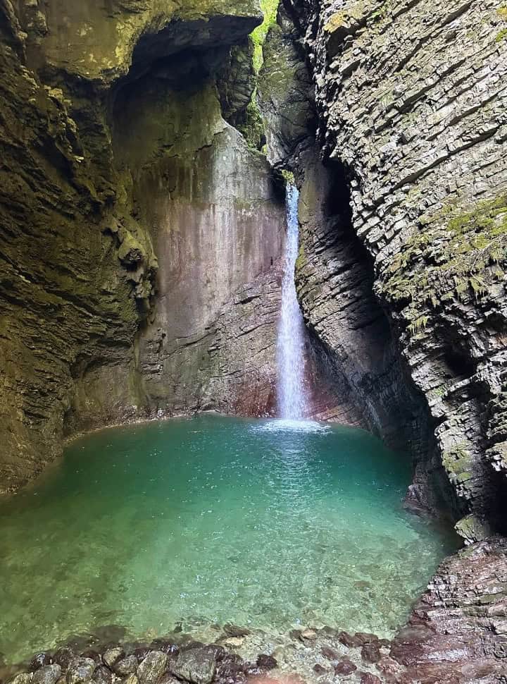 Kozjak waterfall set within a cave falling into a crystal clear water that has a emerald green colour