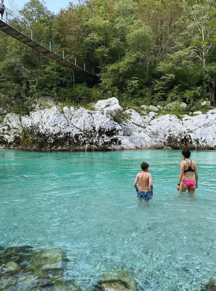 mother and sun wading into the crystal clear bleu water near at the wooden bridge along the slap Kozjak trail Slovenia. 
