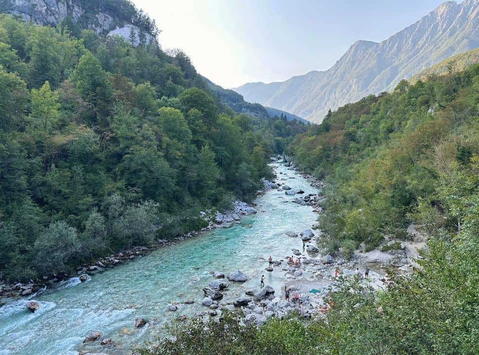 view of a mountain landscape with a river and green valley, people are swimming in the water near Slap Kozjak Slovenia