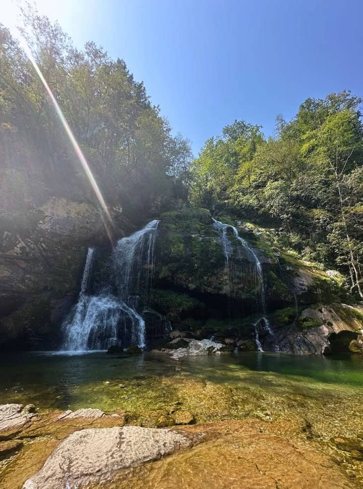 water falling over rocks into the clear crystal waterfall pool, surrounded by forest near Bovec Slovenia. 