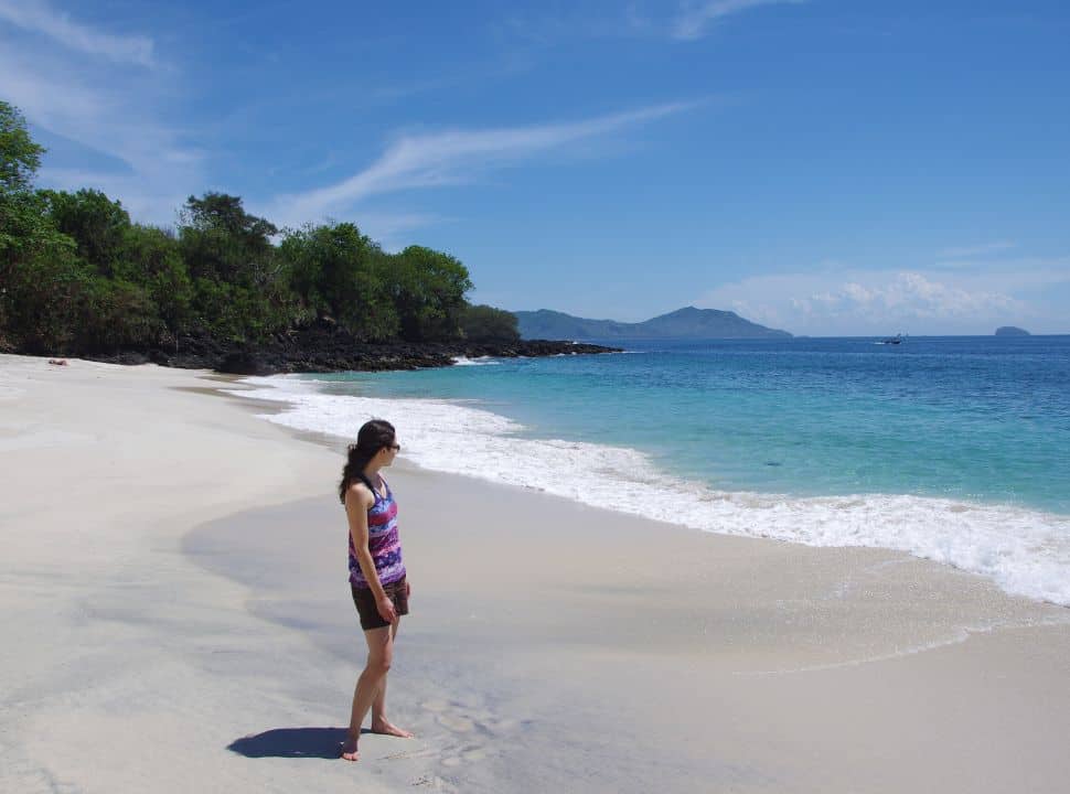 woman standing on a white sanded beach looking at the blue ocean nearby Padangbai