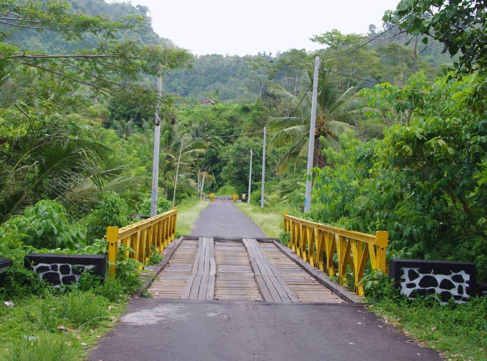 yellow bridge crossing set at a narrow road surrounded by lush vegetation in Sidemen Bali