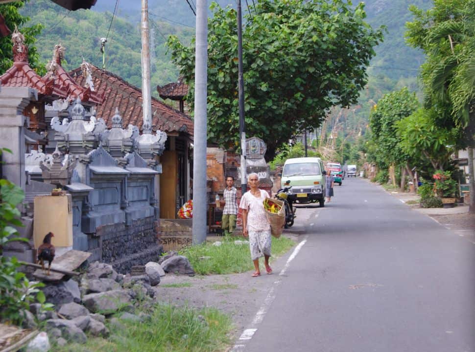 woman walking along the street of a traditional Balinese village, the walls of a temple is visible
