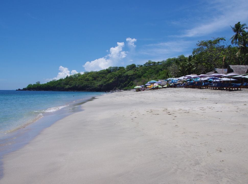 white sanded beach with sun umbrellas and foodstalls. The water is calm and incredibly blue in Bali