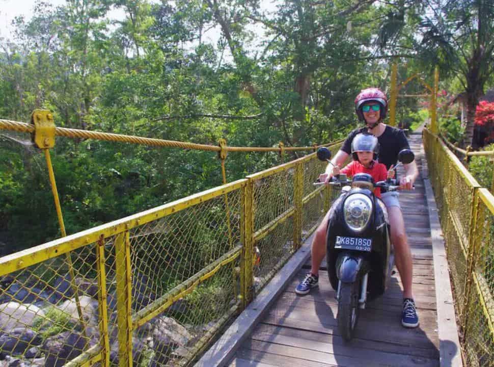 father and son crossing a bright yellow bridge on a motorscooter in Sidemen Bali
