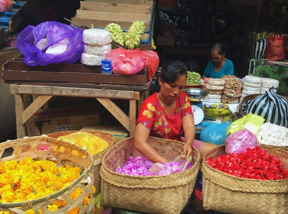 woman putting flower petals in a plastic bag from one of her many basket at the market in Ubud, 