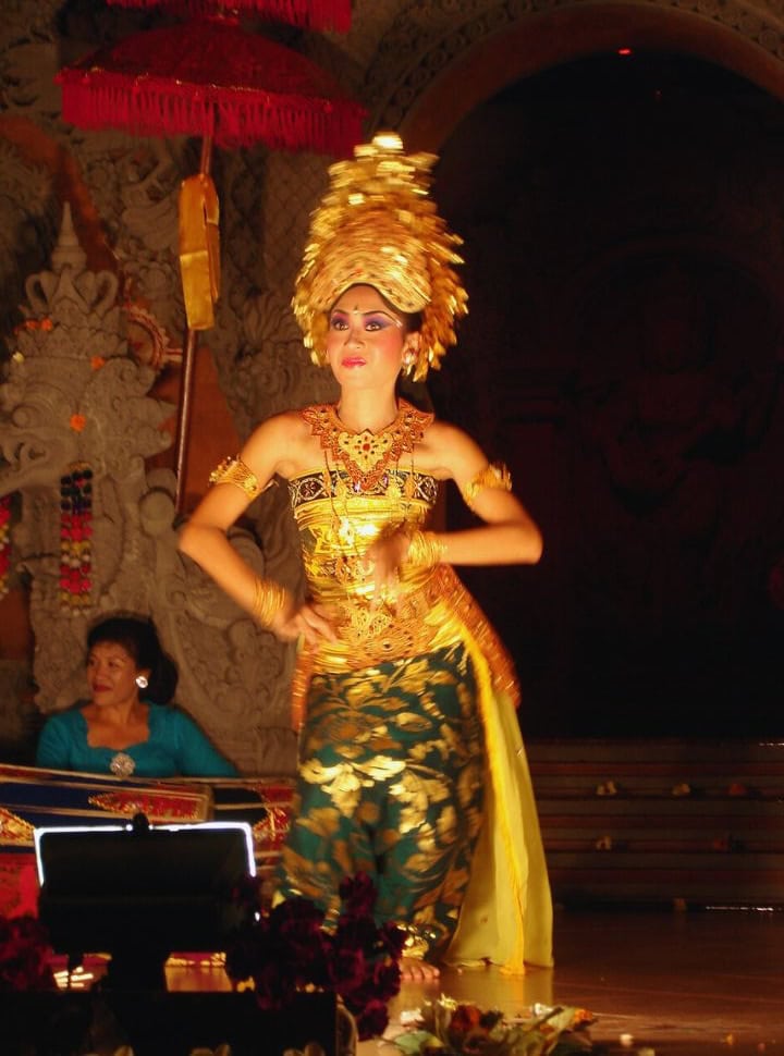 Balinese legong dancer beautifully dressed in golden colored head decoration performing on stage in a Balinese setting