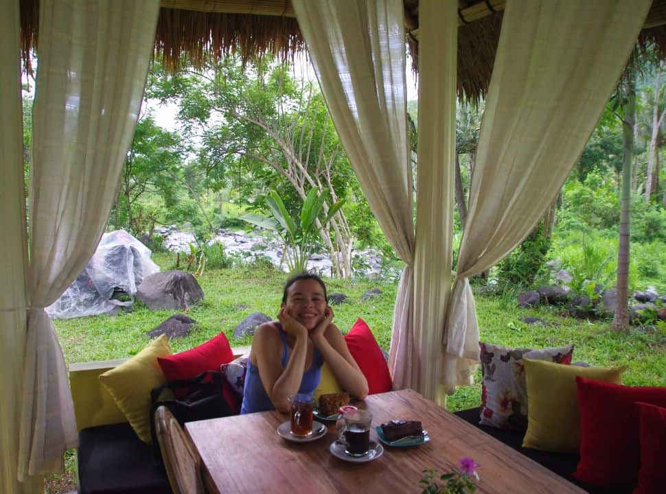 woman sitting in a garden next to a river, ready to eat her cake and drink tea in Sidemen