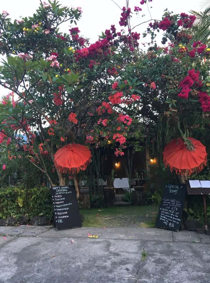 entrance to a restaurant, surrounded by colorful flowers, red umbrellas and a menu written on a black board in Sidemen