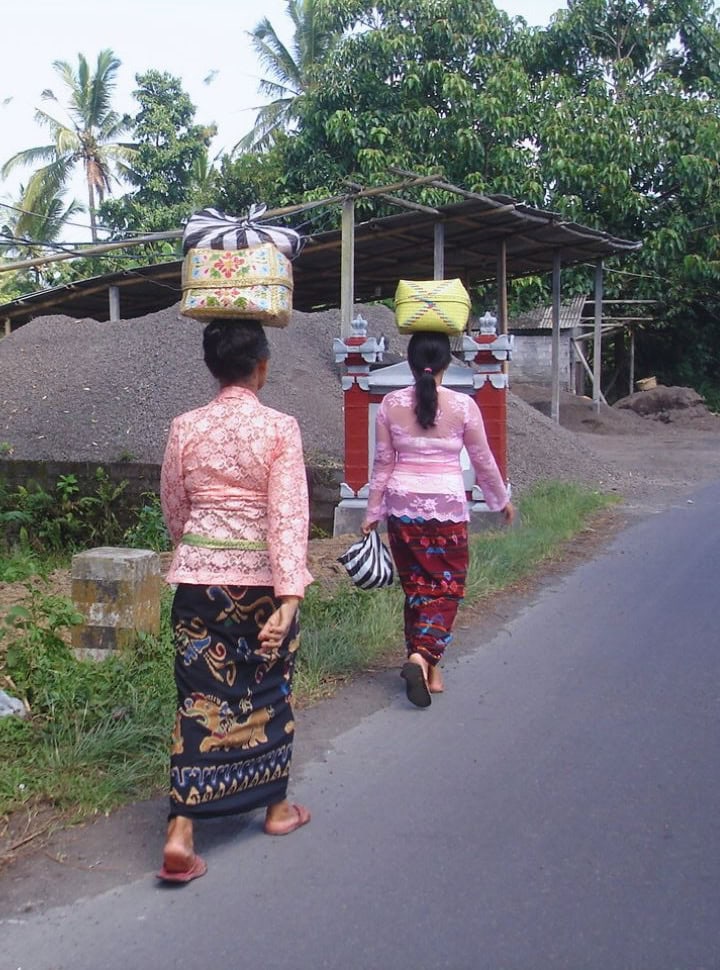women in traditional Balinese clothing balancing a colorful basket on their head while walking along the road in Sidemen Bali