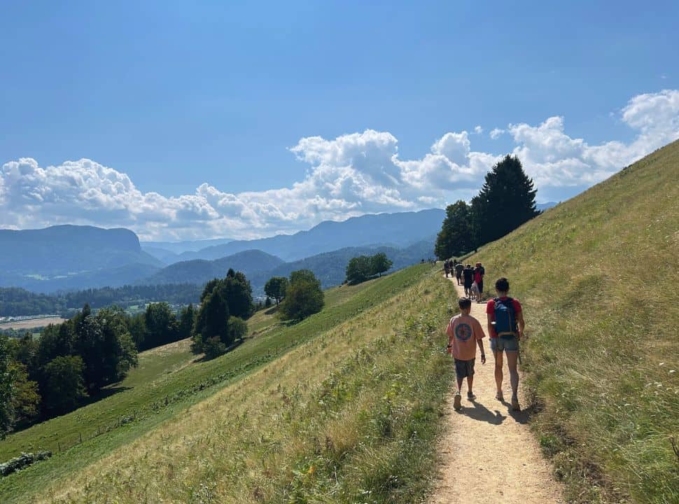 group of people walking along the dusted trail crossing the hill slopes with mountain views in the distance near Vintgar Gorge Slovenia