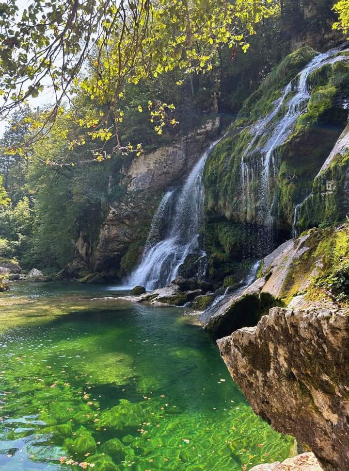 water falling down over several rocks into a calm crystal clear pool in the colour green near Bovec Slovenia. 