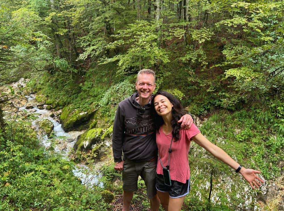 couple posing for a picture in the green lush forest with a crystal clear stream passing in the back at mostnica gorge Slovenia