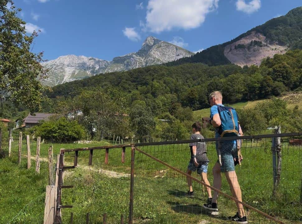 father and son walking along a trail through farm fields with trees with view of a stunning mountain range in Slovenia near Kobarid