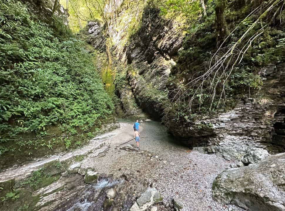 father and son walking along the clear water between a gorge of trees and plants at Kozjak Waterfall Slovenia