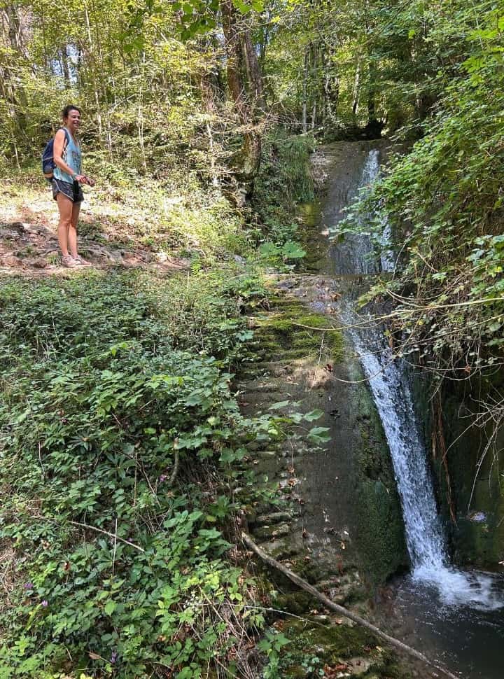 woman standing near a tiny waterfall set within a lush green forest in Slovenia