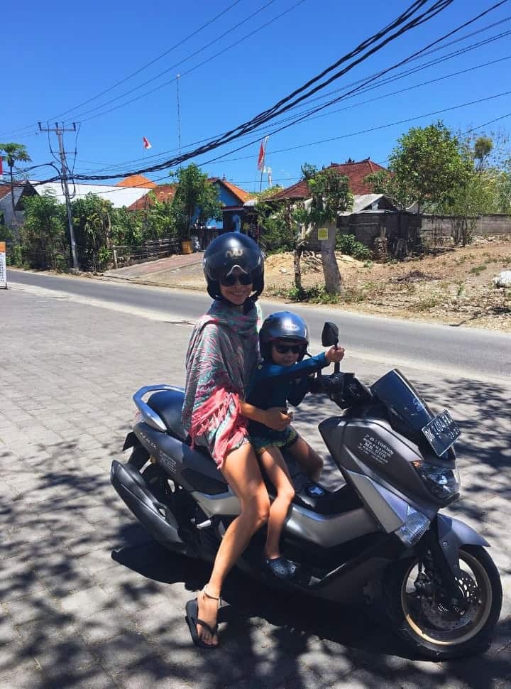 mother and son sitting on a motor scooter along a narrow road in Bali