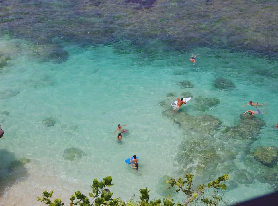 surfer and swimmers enjoying the clear emerald blue green ocean water in the bukit area of south Bali