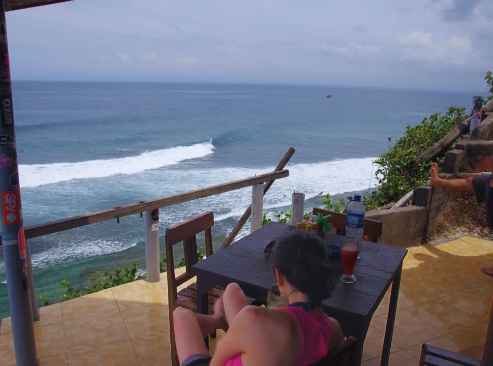 woman sitting high up in a restaurant with view of the ocean with tall waves at Uluwatu Bali
