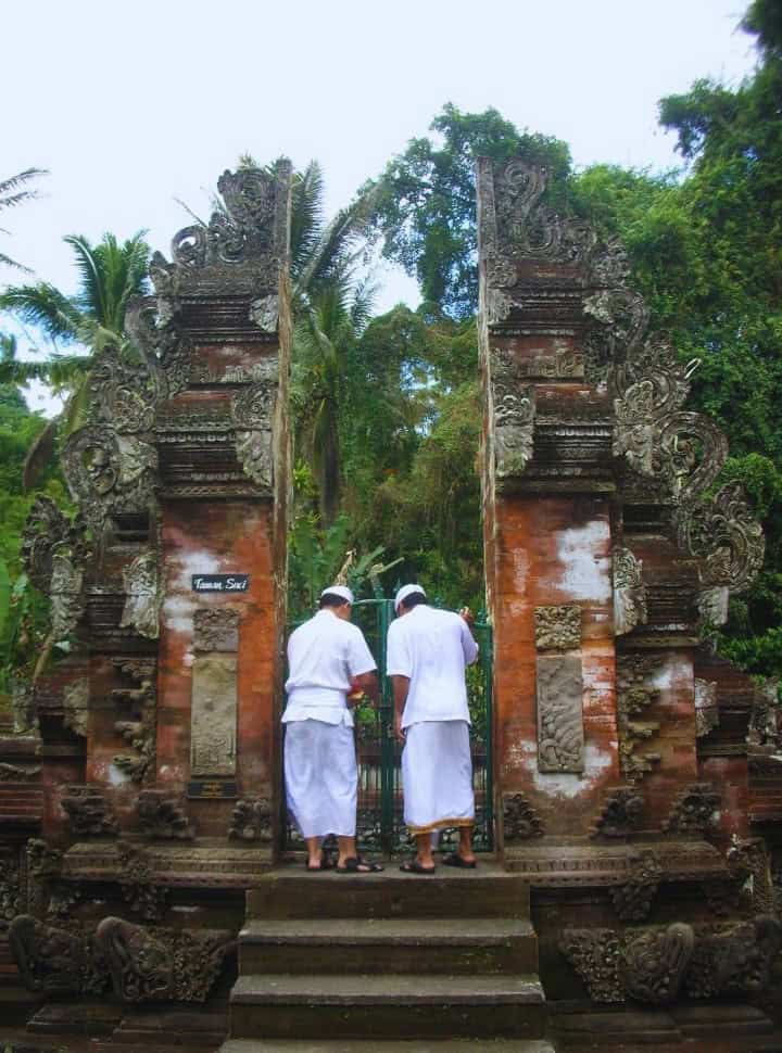 two priests in white standing at a temple gate at tirta empul Bali