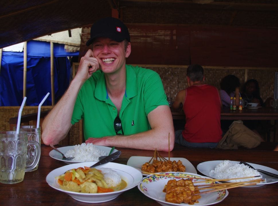 man sitting in a Balinese restaurant with rice, vegetables and sate set on the table