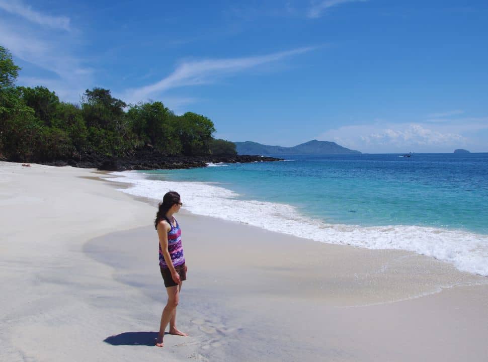 woman standing on a quiet white sanded beach with stunning clear blue water near Padang Bai Bali