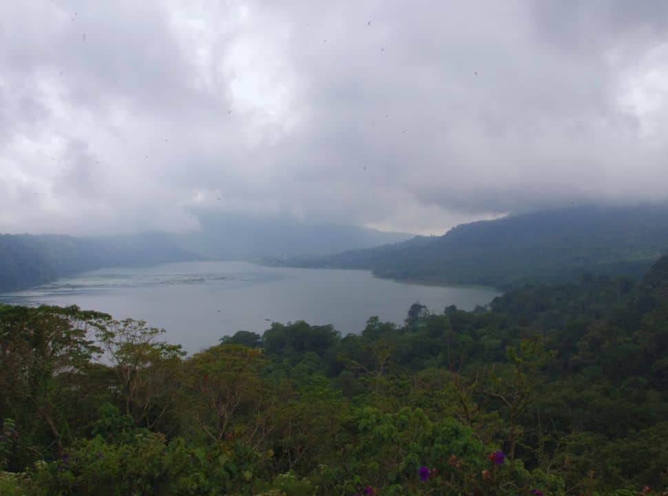 dark clouds hoover over the lake which is surrounded by lush green jungle in north Bali