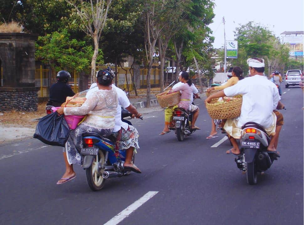 Balinese dressed in beautiful clothing carrying basket on a motorbike along one of the main roads in Bali
