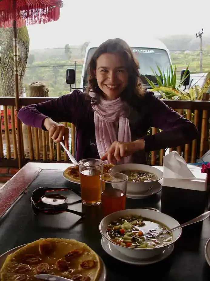 woman sitting at a table in a semi open restaurant with tea, pancakes and hot vegetable soup nearby Munduk Bali