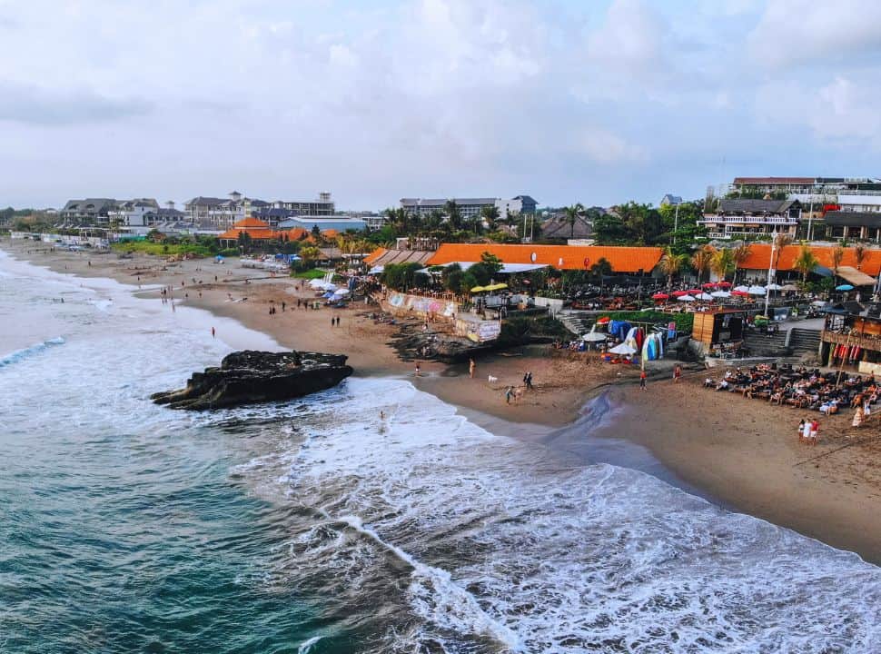 beach bar, umbrellas and people on the beach of Bali at the end of the day, in the back there is a lot of high-rise visible