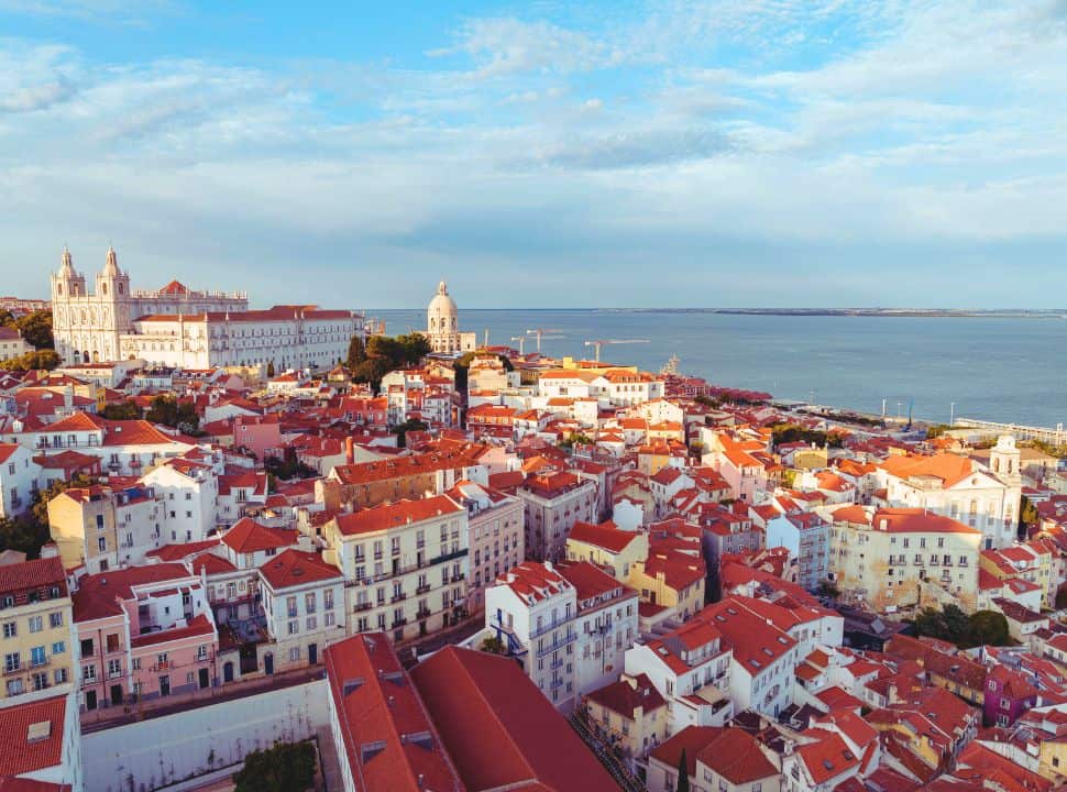 view of Lisbon city with colorful tall and characterful houses along the coast, a cathedral and palace a located higher up. 