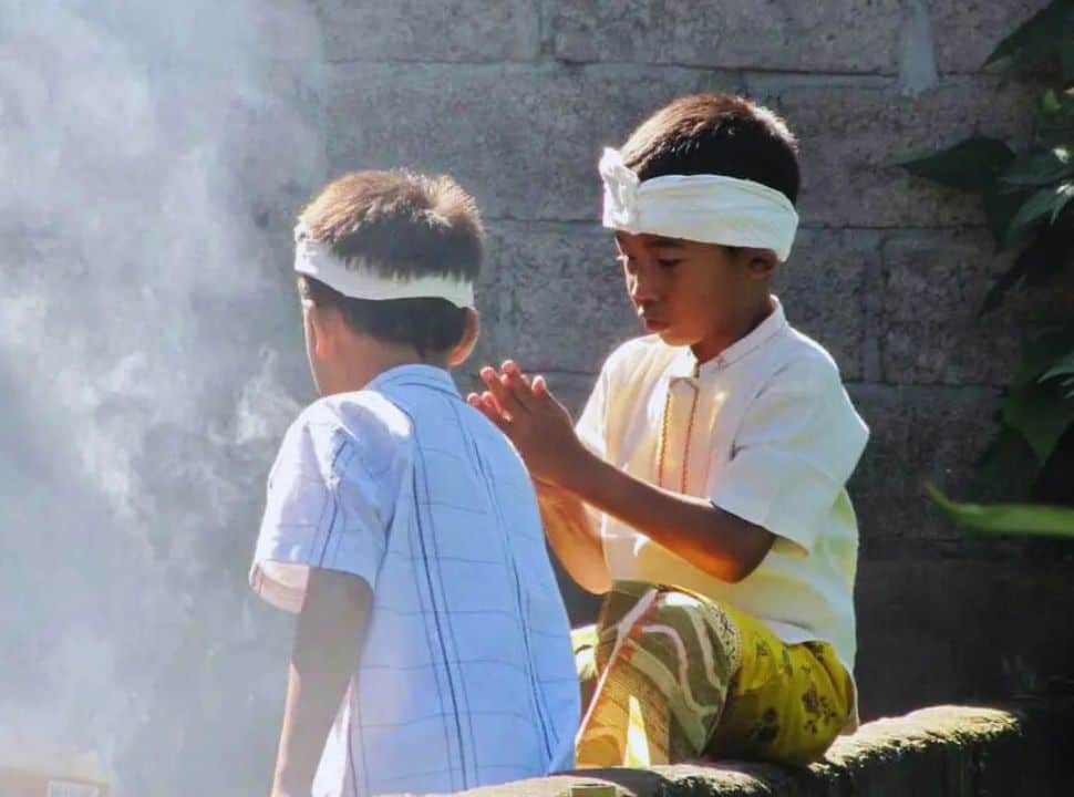 two Balinese kids in nicely dressed with the traditional Balinese head scarf sitting on a wall
