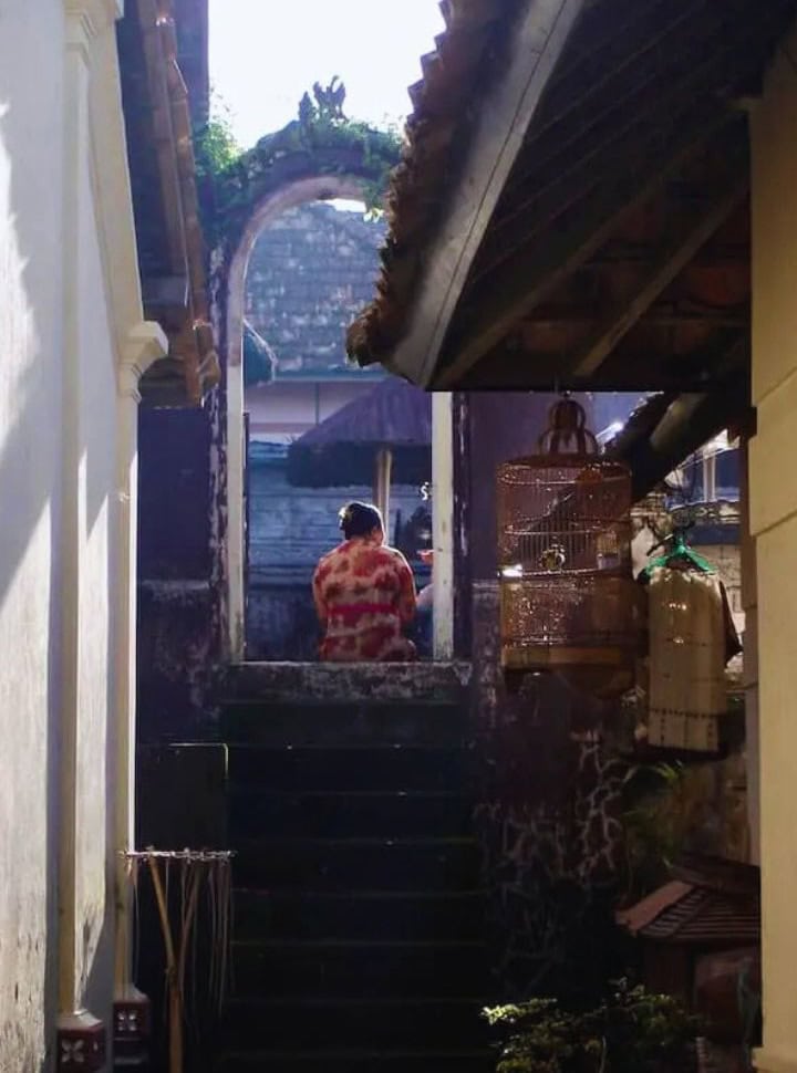 woman sitting in a doorway up the stairs in a narrow alley in Munduk Bali