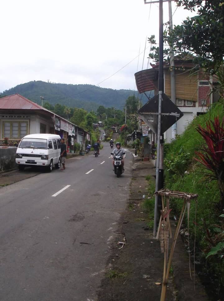 tourist on a motorscooter driving through the street of Munduk along local shops 