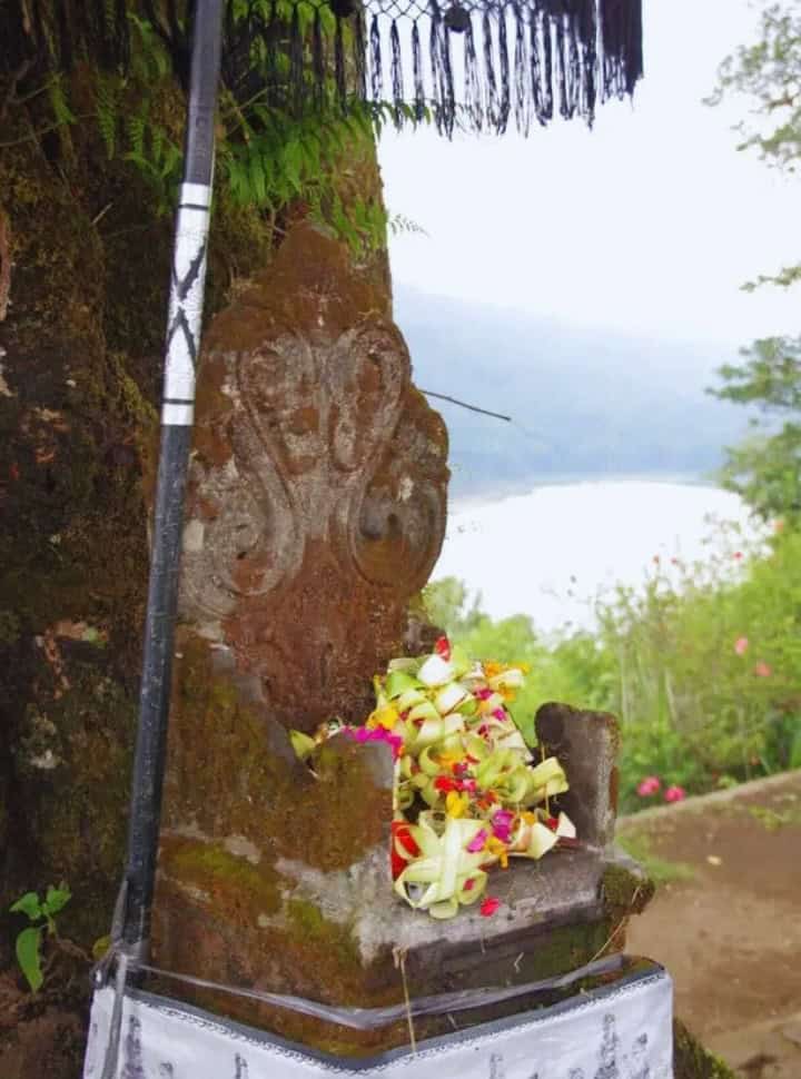 Balinese shrine with colorful offerings set under a Balinese umbrella with in the back view of a lake (Lake Buyan) on the way to Munduk