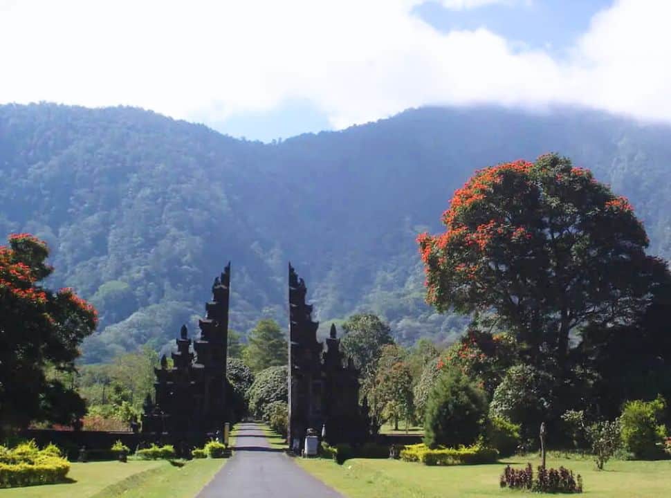 a large temple gate with a long road passing through it, in the back the mountain slopes an beautifully covered with green vegetation nearby Bedugul Bali.
