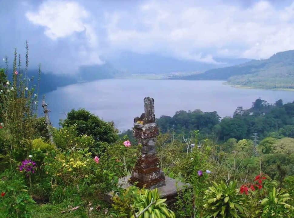 shrine set within a garden with colorful flowers with in the back a view of the lake Buyan Bali